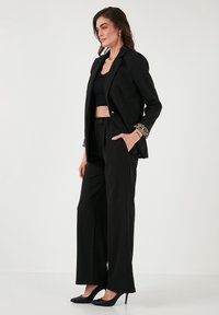 Black blazer with leopard print cuffs, paired with high-waisted black trousers and black heels, featuring a fitted crop top underneath.