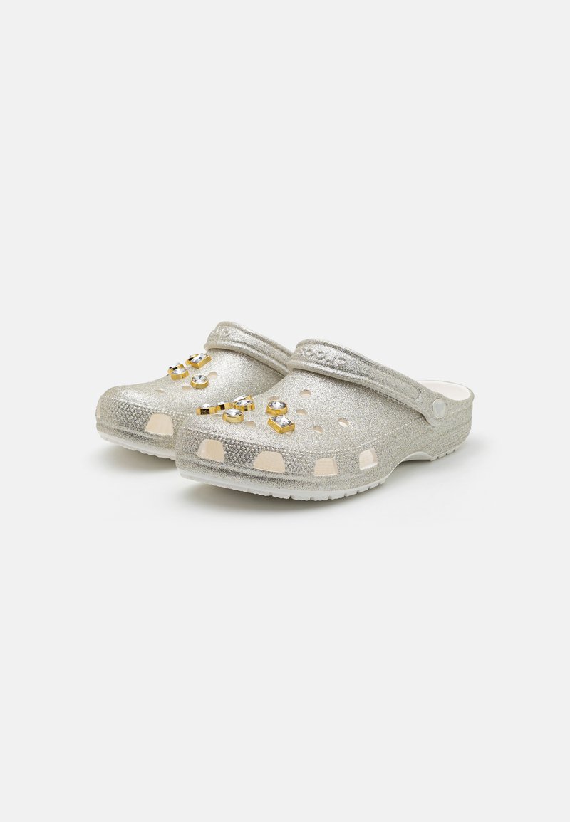 Silberne Holzschuhe mit strukturierten Oberflächen, verziert mit goldenen und klaren dekorativen Akzenten. Offenes Design mit Belüftungslöchern und konturiertem Format.