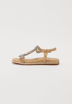 Beżowe płaskie sandały z teksturowaną podeszwą, regulowanym paskiem wokół kostki i dekoracyjnymi kolorowymi akcentami z kamieni szlachetnych wzdłuż górnej części.