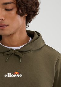Oliwkowy hoodie z troczkiem, z białym logo "ellesse" i akcentem w kształcie półokręgu. Wykonany z miękkiego, gładkiego materiału.