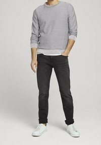Suéter gris a rayas con puños acanalados, combinado con jeans negros ajustados y zapatillas blancas. El conjunto presenta un estilo en capas con una camiseta blanca debajo.