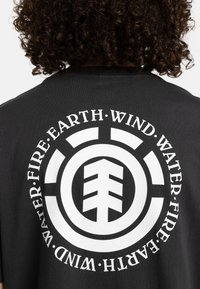 Zwart katoenen T-shirt met een groot wit grafisch ontwerp, cirkelvormig met een boom symbool in het midden en de woorden "WATER, VUUR, AARDE, WIND" eromheen.