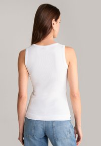 Top bianco a costine senza maniche con scollo rotondo e una silhouette aderente, abbinato a jeans in denim azzurro chiaro con cuciture in vista.