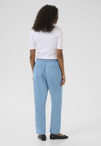 Lyseblå denimbukser med løs pasform, elastisk talje, to baglommer og opsmøgede hems. Matchet med en hvid top med korte ærmer.