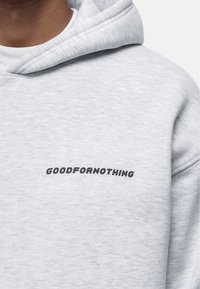 Felpa grigia chiara realizzata in tessuto morbido, con un logo nero "GOODFORNOTHING" sulla parte anteriore. Progettata con cappuccio regolabile tramite cordino e polsini a coste.