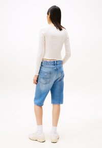 Hvit langermet topp med bølgede kanter, sammen med blå denimshorts, med en avslappet passform og to baklommer.