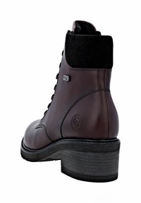 Botín de piel marrón con un cuello de tela negra texturizada, puntera redondeada, parte frontal con cordones y un tacón bajo y cuadrado.