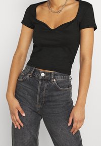 Svart ribbad kortärmad topp med sweetheart-urringning, kombinerad med högmidjade mörka denimjeans med knappstängning och klassiska fickor.