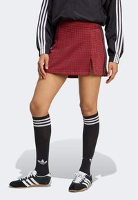Red patterned skort with a side slit, paired with black knee socks featuring white stripes and black and white athletic shoes.