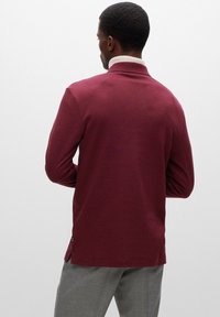 Langärmliges, burgunderrotes Poloshirt mit einem gerippten, weißen Kragen. Weicher Stoff, seitliche Schlitze am Saum und eine lockere Passform.