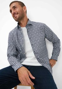 Langarmhemd mit einem marineblauen und weißen Paisleymuster, Button-Down-Kragen und einer lockeren Passform, getragen über einem weißen T-Shirt.