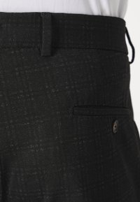 Pantalons à motif carreaux noirs en tissu texturé, dotés d'une fermeture par bouton et d'une poche latérale. Coupe ajustée avec une taille plate.