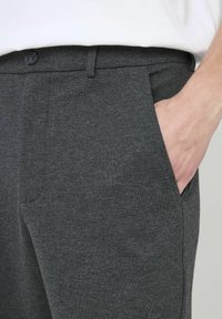 Pantalon gris foncé en tissu doux, au coupe classique, avec des poches avant et une taille lisse ornée d'un bouton noir.
