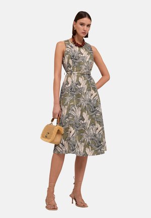 Mouwloze jurk met bloemenpatroon in olijfgroen, aansluitend op de taille, gecombineerd met een kleine rieten handtas en beige sandaletten.