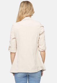 Lichtroze blazer met een getailleerde pasvorm, opgerolde mouwen en subtiele naden, gecombineerd met blauwe jeans. Geen zichtbare logo's of patronen.