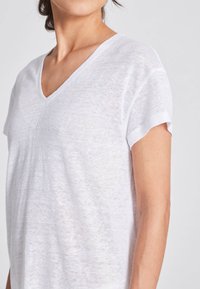 Vit V-ringad t-shirt i lätt, något genomskinlig tyg med korta ärmar och en avslappnad passform, som visar en minimalistisk design.