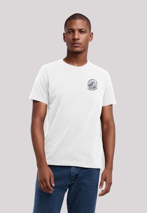 Weißes Baumwoll-T-Shirt mit kurzen Ärmeln und rundem Ausschnitt, mit einem schwarzen Grafikdruck auf der linken Seite. Getragen mit dunkelblauen Jeans.