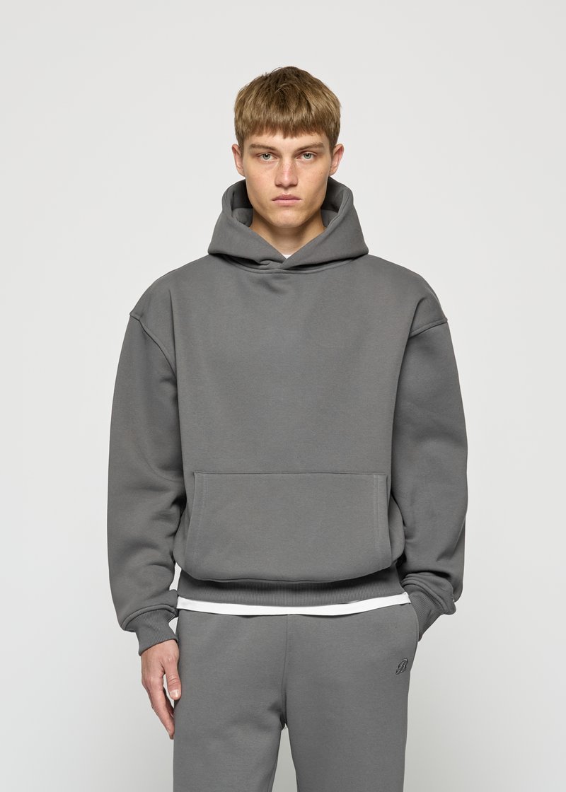 Gray hoodie with a spacious kangaroo pocket, ribbed cuffs, and hem. Soft fabric, relaxed fit, and a large hood. Paired with gray pants.