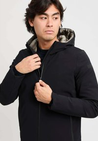 Giacca nera isolante con zip frontale e un rivestimento interno a fantasia. Presenta un cappuccio ed è realizzata in un materiale liscio e resistente.
