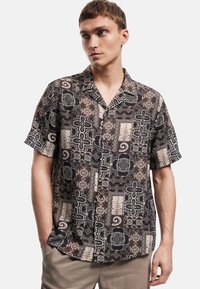 Kurzärmeliges, knöpfbares Hemd aus gemustertem Stoff in Dunkelbraun mit weißen geometrischen Designs und Akzenten. Verfügt über eine lässige Passform.