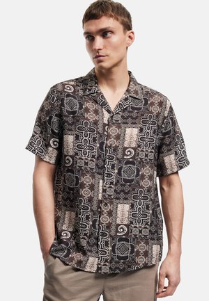 Camisa de manga corta abotonada, hecha de tela estampada en marrón oscuro con diseños geométricos blancos y acentos. Presenta un ajuste holgado.