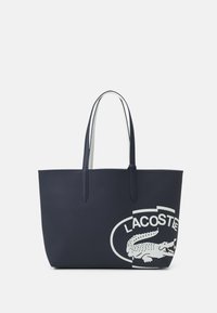 Sac cabas bleu marine à doubles poignées, fabriqué en matériau texturé. Présente un grand logo Lacoste blanc avec une illustration de crocodile.
