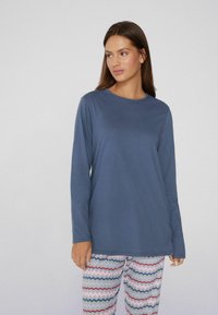 Langemouwen blauwe top van zachte stof, met een ronde halslijn. Gecombineerd met pyjamabroek met een patroon van golvende roze, blauwe en grijze strepen.