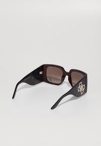 Gafas de sol marrón carey con lentes cuadrados de gran tamaño, brazos texturizados negros y un logotipo decorativo metálico en el costado.
