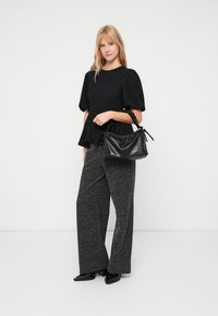 Top peplum preto em tecido texturizado, calças largas cinza com padrão e uma pequena bolsa preta com fecho de cordão. Sapatos pretos.