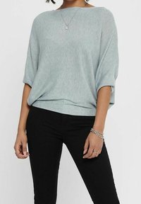 Jasnoniebieski, oversize'owy sweter z krótkimi rękawami, o prążkowanej fakturze i łódkowym dekolcie, zestawiony z dopasowanymi czarnymi jeansami.