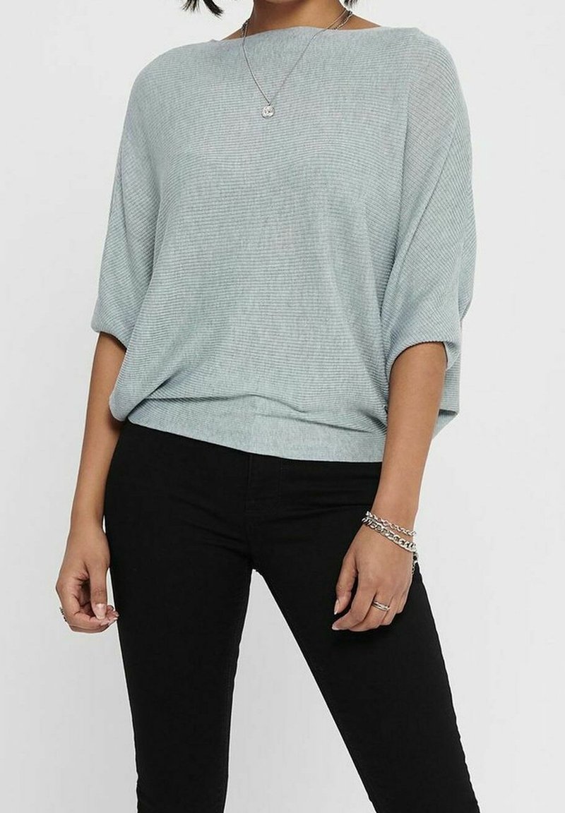 Jasnoniebieski, oversize'owy sweter z krótkimi rękawami, o prążkowanej fakturze i łódkowym dekolcie, zestawiony z dopasowanymi czarnymi jeansami.