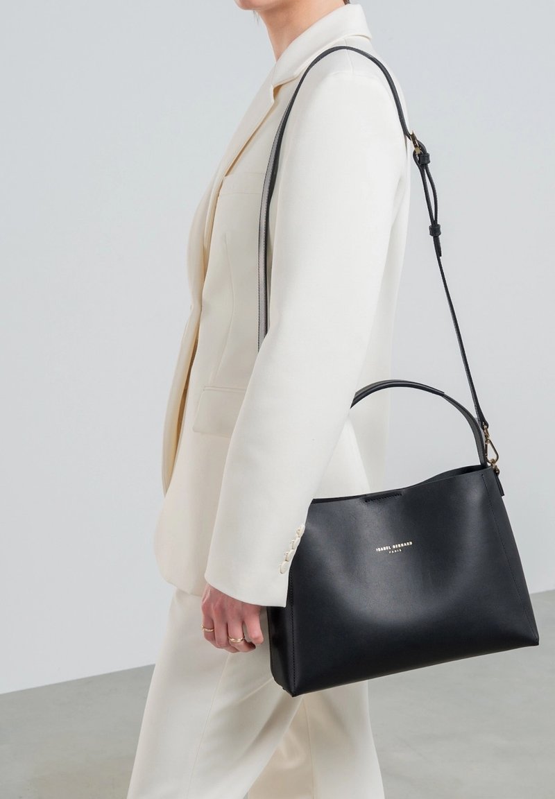 Sac à main en cuir noir au design structuré, avec une poignée supérieure et une bandoulière détachable. Présente un logo argenté à l'avant.