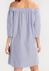 Off-shoulder klänning i blå och vita vertikala ränder. Tre fjärdedels ärmar, elastisk halsringning, lätt bomullstyg. Avslappnad passform.