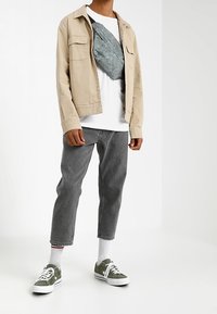 Chaqueta beige sobre camiseta blanca con una bolsa de patrones azul claro, jeans grises y zapatillas verdes, completado con calcetines blancos.