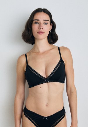Zwarte bralette met kantafwerking, zachte cups en dunne bandjes, gecombineerd met bijpassende zwarte onderbroeken met kant, met een delicate strikaccent.
