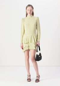 Rochie galbenă cu un model, cu mâneci lungi, guler înalt, talie peplum și tiv ondulat. Asortată cu o geantă de umăr neagră, matlasată, și sandale cu barete.