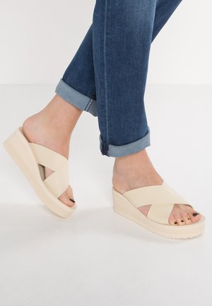Beżowe sandały na koturnie z krzyżującymi się paseczkami, o fakturowanym wykończeniu i gumowej podeszwie, z otwartym noskiem i niskim obcasem.