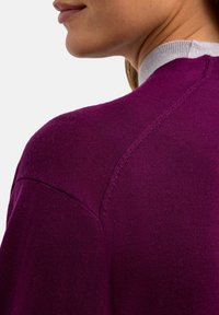 Pull en tricot violet avec un col rond et des accents gris clair au niveau du col. Présente un design d'épaule sans couture et un tissu texturé.