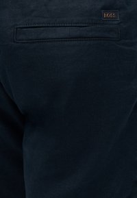 Σκούρο ναυτικό ύφασμα με τσέπη welt και μικρή ορθογώνια καφέ ετικέτα λογότυπου BOSS πάνω από την τσέπη.