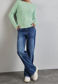 Mint green, fluffy knit sweater with an off-shoulder design paired with blue wide-leg jeans and white sneakers on a gray background.