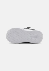 Baskets noir et blanc avec une semelle en caoutchouc texturé, une sangle Velcro et un design minimaliste. La semelle présente un motif en nid d'abeille pour une meilleure adhérence.
