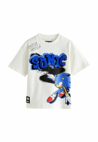 Biała bawełniana koszulka z niebieskim napisem "SONIC" oraz grafiką jeża Sonika w akcji, z czerwonymi detalami butów i czarnymi akcentami.