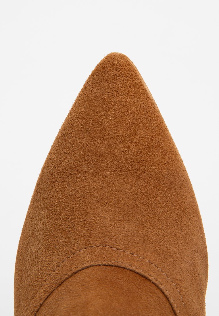 Punta di una scarpa in camoscio marrone con cuciture visibili su uno sfondo bianco.