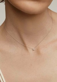 Collar de plata con una cadena delicada y un pequeño colgante en forma de flor que presenta una piedra central, llevado cerca de la clavícula.