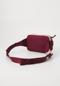 Bordo tkanina torba na rame s ružičastim patentnim zatvaračem i podesivim remenom, s pravokutnim oblikom i dizajnerskim šavovima.