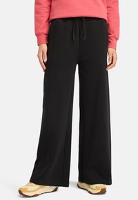 Svarta vida sweatpants med elastisk midja, dragsko och sidofickor. Matchat med gula och blå träningsskor.