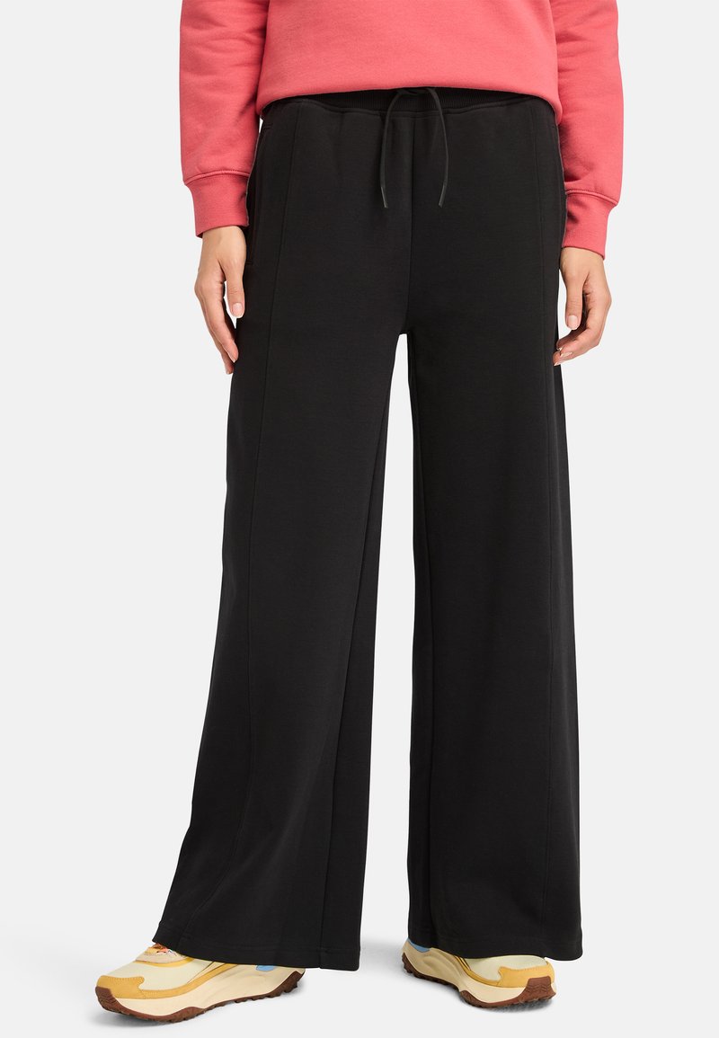 Svarta vida sweatpants med elastisk midja, dragsko och sidofickor. Matchat med gula och blå träningsskor.