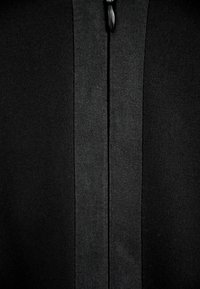 Czarny materiał z bliska, z centralnym zamkiem błyskawicznym o teksturowanym wykończeniu i gładkich krawędziach, tworzącym bezszwowy design.