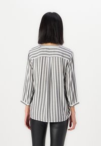 Stripet bluse i grått og hvitt stoff med trekvart ermer, avrundet hem og en bakfold for ekstra tekstur.