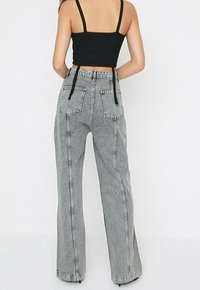 Crop top noir avec des fines bretelles associé à un jean en denim gris taille haute et à jambe large, doté de poches arrière et de détails de couture visibles.